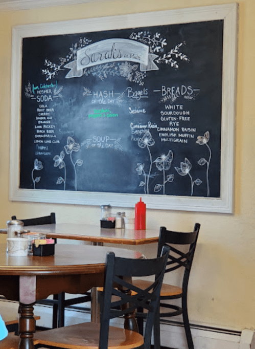 Chalkboard menu at Sarah's on Main featuring daily specials, bagels, breads, and condiments on a table.