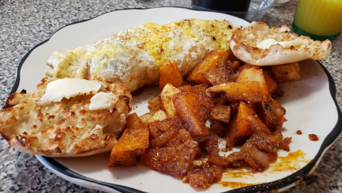 A plate with a fluffy omelette, roasted potatoes, and toasted English muffins topped with butter.
