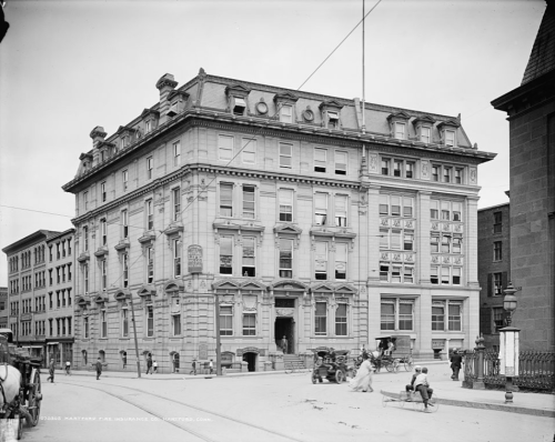Historic building with ornate architecture, featuring large windows and a busy street scene in front. Black and white photo.