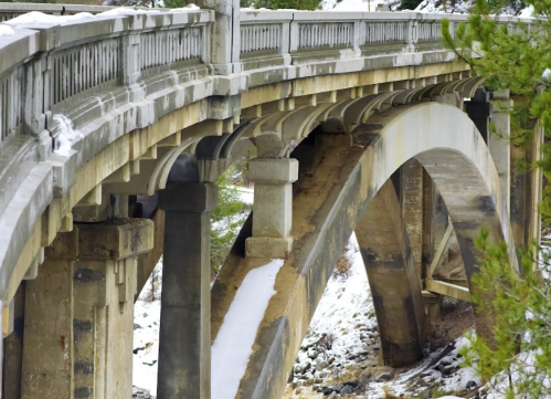 A close-up view of a stone bridge arching over a snowy landscape, showcasing its architectural details and supports.