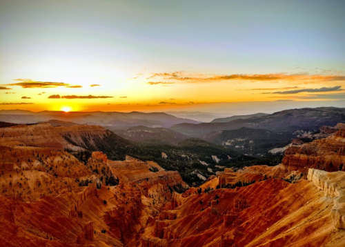 Sunset over a mountainous landscape with layered rock formations and a colorful sky.