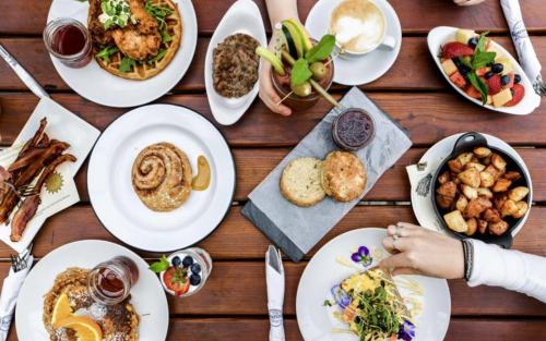 A table spread with various brunch dishes, including waffles, fruit, pastries, and drinks, arranged beautifully.