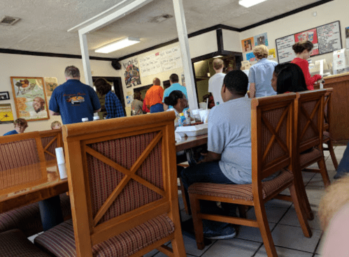 A busy restaurant interior with people in line and seated at wooden tables, enjoying their meals.