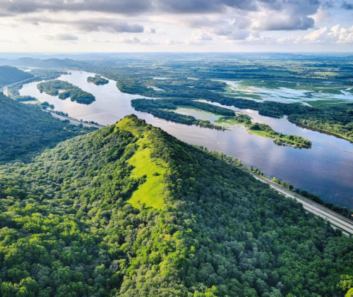 Aerial view of lush green hills and winding rivers under a cloudy sky, showcasing a vibrant natural landscape.