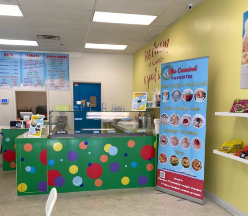 Brightly colored ice cream shop interior with a service counter, menu banner, and snacks displayed on shelves.