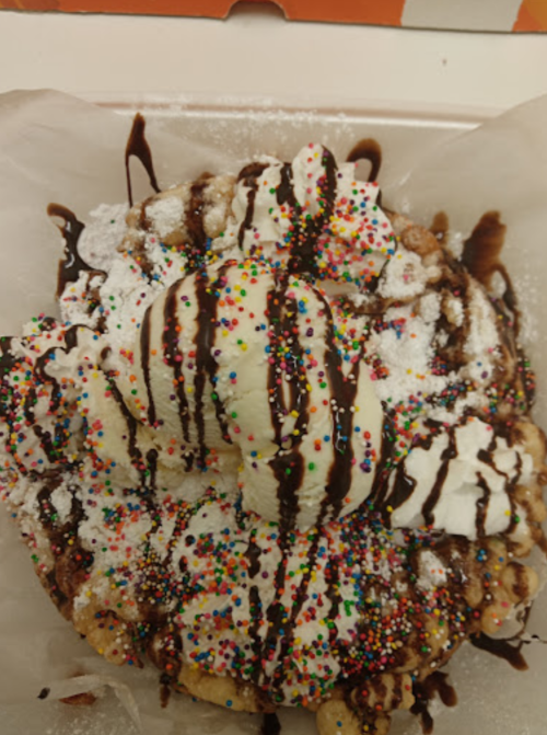 A dessert topped with ice cream, chocolate drizzle, whipped cream, and colorful sprinkles on a bed of fried dough.