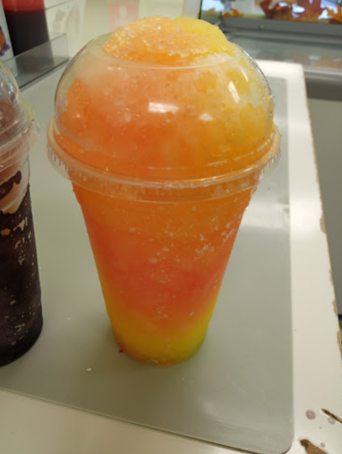 A colorful frozen drink in a clear cup, featuring layers of orange, yellow, and green slushy ice.