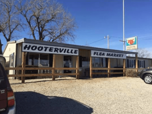 Exterior of Hooterville Flea Market, featuring a sign and wooden fence, under a clear blue sky.