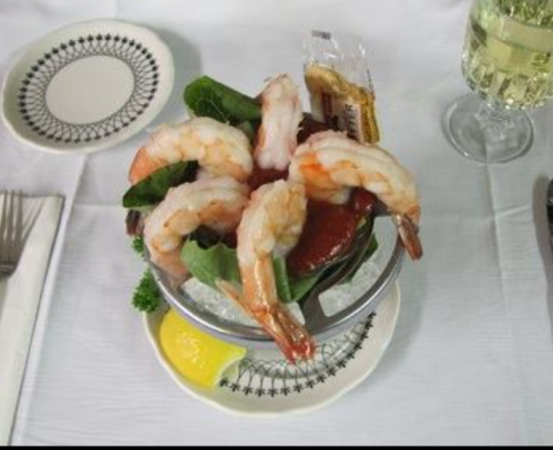 A seafood dish featuring shrimp on ice, served with cocktail sauce, lemon, and a garnish on a decorative plate.