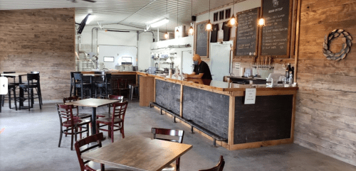 A rustic bar area with wooden tables and a bartender serving drinks in a cozy, well-lit space.