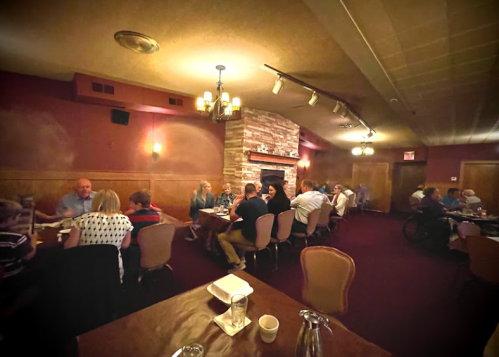 A dimly lit restaurant interior with diners at tables, featuring a stone fireplace and warm decor.