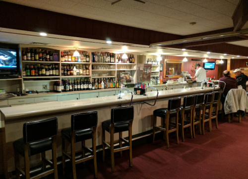 A well-stocked bar with high stools, a bartender, and a TV in a cozy, dimly lit setting.
