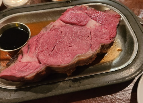 A large, juicy prime rib served on a metal platter with a small cup of dark sauce on the side.