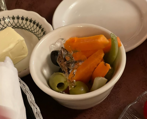 A small bowl of mixed vegetables, including carrots, celery, and olives, with ice cubes on top.