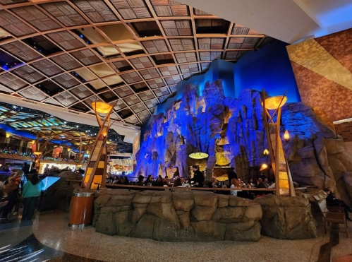 Interior of a vibrant restaurant with rock formations, blue lighting, and a high ceiling, filled with diners.