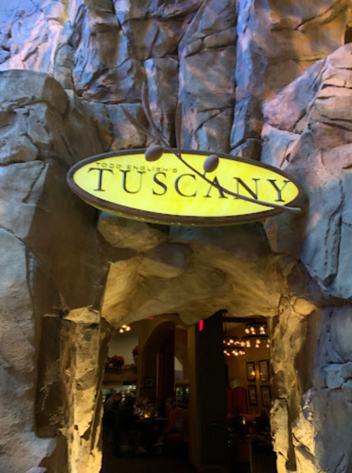 Sign for "Tuscany" restaurant, set against a rocky, cave-like entrance with warm lighting.