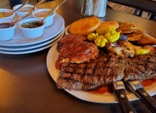 A plate of grilled meats, including ribs and chicken, served with sides and sauces on a table.