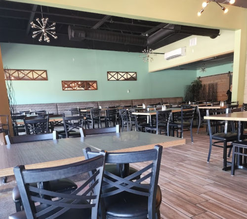 Interior of a restaurant with empty tables and chairs, featuring green walls and modern light fixtures.