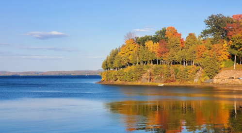 A serene lake scene with colorful autumn trees reflecting on the water under a clear blue sky.