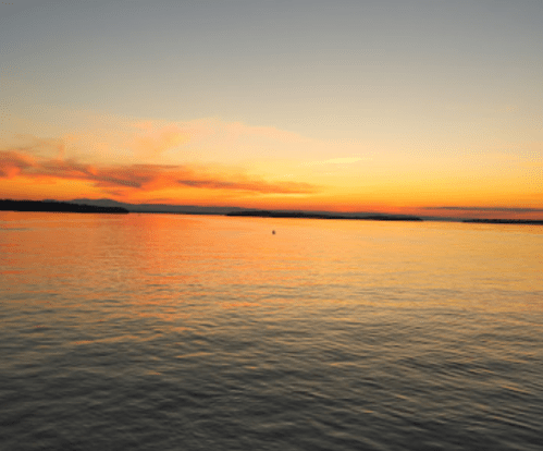 A serene sunset over calm waters, with vibrant orange and pink hues reflecting on the surface.