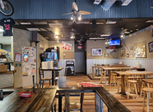 Interior of a casual restaurant with wooden tables, ceiling fans, and wall decor, featuring a bar area and TV.
