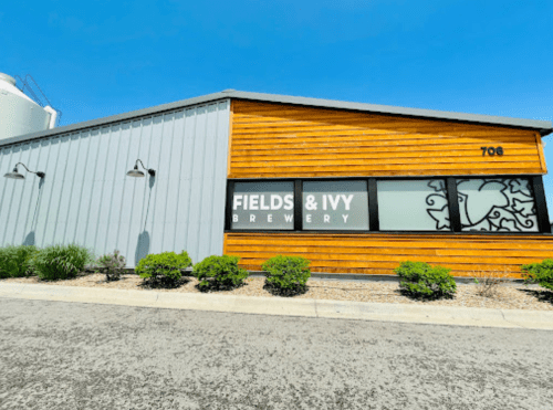 Exterior of Fields & Ivy Brewery, featuring a wooden facade and large windows, under a clear blue sky.