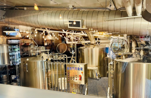 A modern brewery interior featuring large stainless steel tanks and industrial decor with warm lighting.