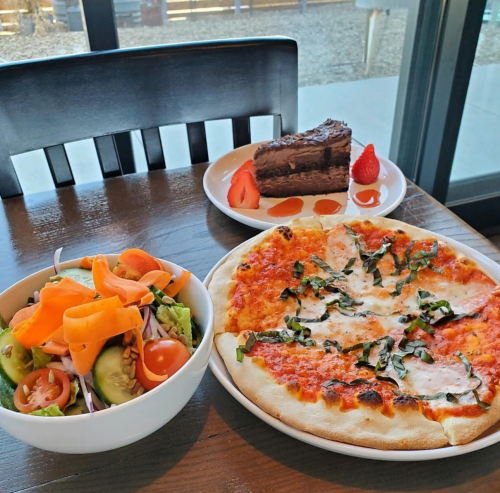 A table with a pizza, a salad with vegetables, and a slice of chocolate cake with strawberries.