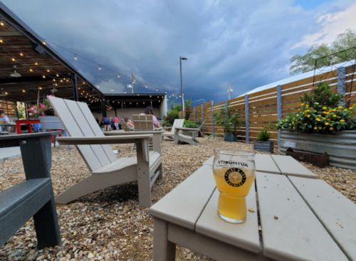 A glass of beer sits on a table in a cozy outdoor space with string lights and stormy skies in the background.