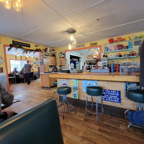 A cozy diner interior with wooden floors, a counter, and colorful decor, featuring patrons and vintage signs.