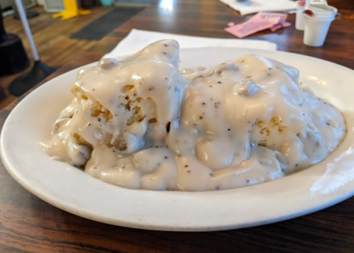 A plate of biscuits smothered in creamy sausage gravy, served in a casual dining setting.