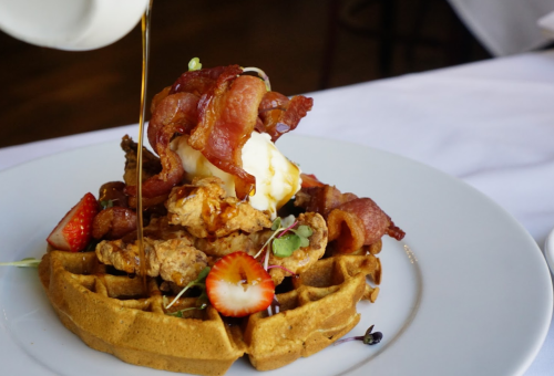 A plate of waffles topped with fried chicken, bacon, strawberries, and drizzled with syrup.