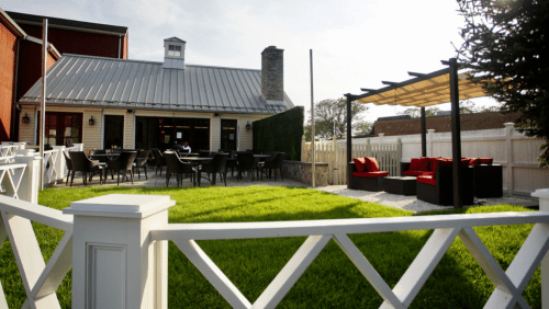 A cozy outdoor seating area with a lawn, patio furniture, and a shaded pergola beside a charming building.