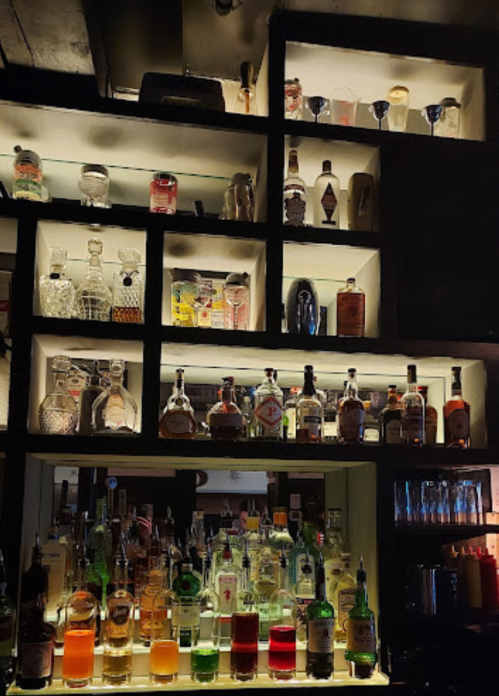 A well-stocked bar with various bottles of liquor and colorful cocktails displayed on shelves.