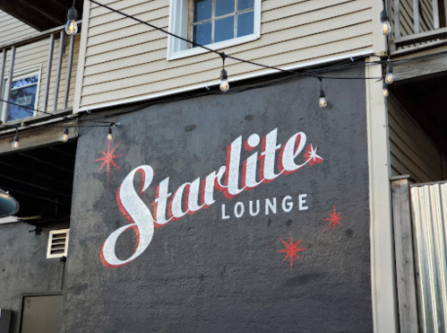 A wall featuring the painted sign "Starlite Lounge" with decorative stars and string lights above.