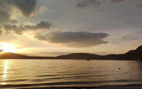 Sunset over a calm lake, with mountains in the background and clouds reflecting warm colors in the sky.