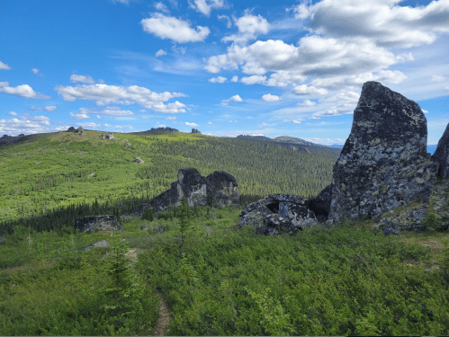 A scenic view of rocky formations amidst lush green hills under a blue sky with scattered clouds.