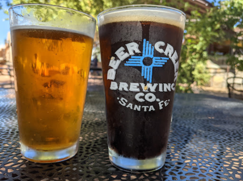 Two glasses of beer on a table: one light golden and one dark, both featuring the logo of Beer Creek Brewing Co.