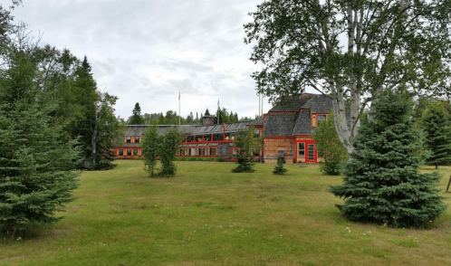 A large, rustic building surrounded by trees and grassy areas under a cloudy sky.