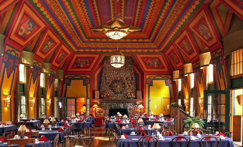 Colorful dining room with vibrant patterned walls, a stone fireplace, and tables set for guests.