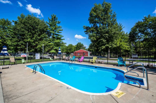A clear blue swimming pool surrounded by green trees and colorful lounge chairs on a sunny day.