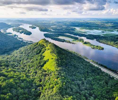 Aerial view of lush green hills and winding rivers under a cloudy sky, showcasing a vibrant natural landscape.