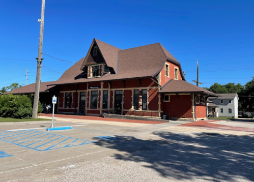 Historic red train station with a steep roof and large windows, set against a clear blue sky.