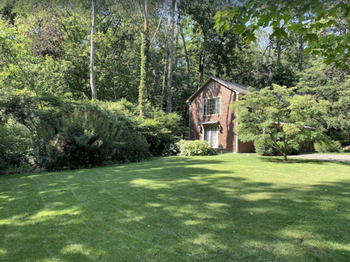 A brick house surrounded by lush greenery and trees, set on a well-maintained lawn.
