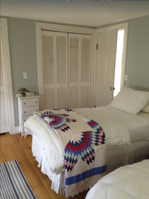 A cozy bedroom with two beds, a colorful quilt, and light-colored walls. A closet and door are visible in the background.