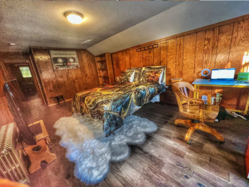 A cozy wooden room featuring a bed with patterned bedding, a desk with a computer, and a chair, all on a cloud-like floor.