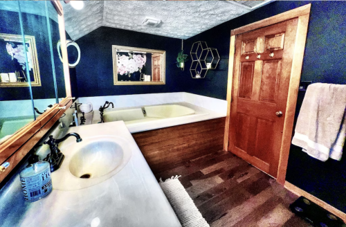 A stylish bathroom featuring a wooden tub, dark blue walls, a sink, and a wooden door with decorative accents.
