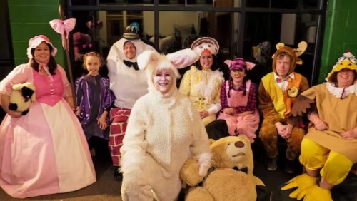 A group of people in colorful costumes, including a bunny, sheep, and various animal characters, posing together.