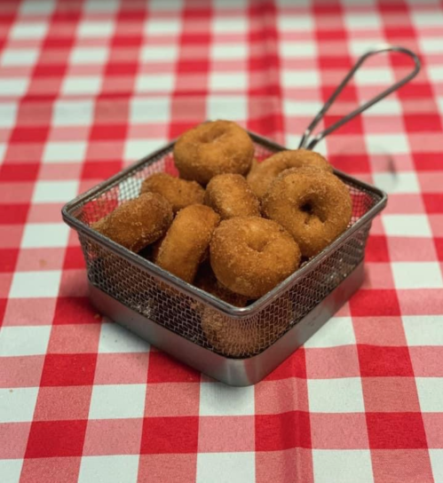 A small metal basket filled with golden-brown donuts, resting on a red and white checkered tablecloth.