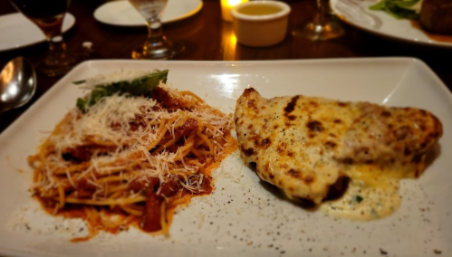 A plate featuring pasta with marinara sauce and cheese, alongside a baked chicken breast with a creamy sauce.